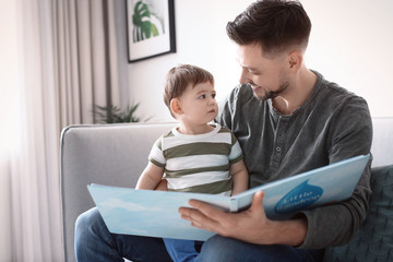 Fototapeta premium Dad and his son reading book on sofa at home