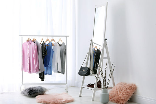 Rack with clothes and modern mirror in light room