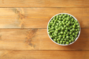 Bowl with green peas on wooden background, top view