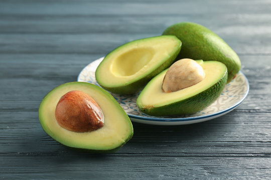 Plate with ripe avocados on wooden background