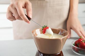 Woman dipping ripe strawberry into bowl with white chocolate fondue on table