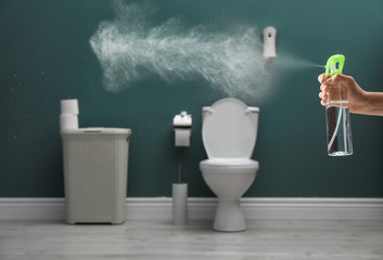 Woman spraying air freshener in bathroom