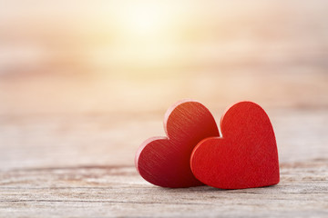 Fototapeta premium Two red hearts on wooden background in sunset