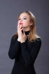 Portrait of a girl in black clothes, wet hair, holding hands on her face, eyes closed. Studio shot, against a gray background