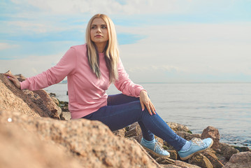 Fototapeta na wymiar Beautiful girl near the sea. in the lotus position near the stones on the shore. relaxing nature water and sky.
