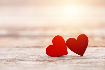 Obraz premium Two red hearts on wooden background in sunset