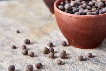 Black sesame seeds in a clay bowl with scattered seeds on wooden barrel, close-up, shallow depth of field.