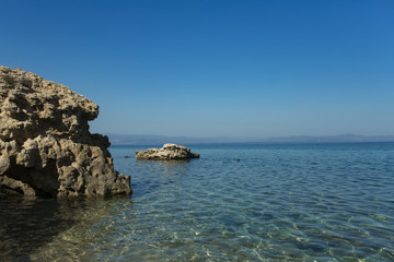 Stony shore on idyllic seascape. Rock in sea water on sunny blue sky. Wild nature, environment and ecology. Holiday destination and travelling. Summer vacation and wanderlust