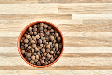Clay bowl with dried allspice berries on textured wooden background, top view, close-up, macro, selective focus.