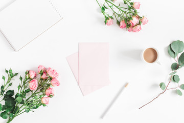 Office desk with notebook, rose flowers, eucalyptus branch, pink paper blank. Flat lay, top view, copy space