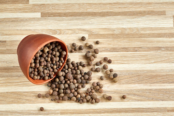 Overturned clay bowl with dried allspice berries on textured wooden background, close-up, macro, selective focus.