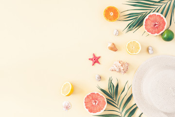 Summer composition. Fruits, hat, tropical palm leaves, seashells on pastel yellow background....