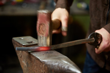 Close-up of a blacksmith's hands manipulating a metal piece above his forge, selective focus.