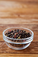 Front view of peppercorn in glass bowl on wooden background, close-up, shallow depth of field, vertical.