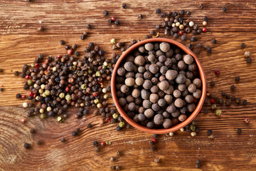 Clay bowl with pimento and peppercorns on vintage wooden background, top view, close-up, macro, selective focus.