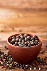 Close-up of clay bowl with pimento and peppercorn on vintage wooden background, macro, shallow depth of field.