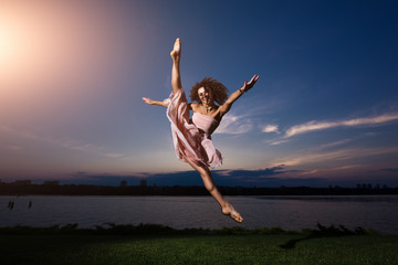 Young flexible ballerina in dress make splits against evening sky