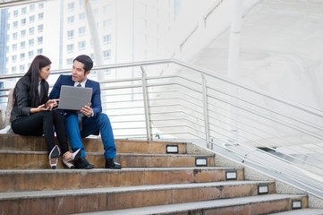 Asian businesswoman and businessman sit on the staircase with laptop. concept of sale report and marketing plan for the future with copy space for text.