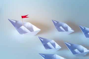 Leadership concept using  paper ship with red flag on blue background