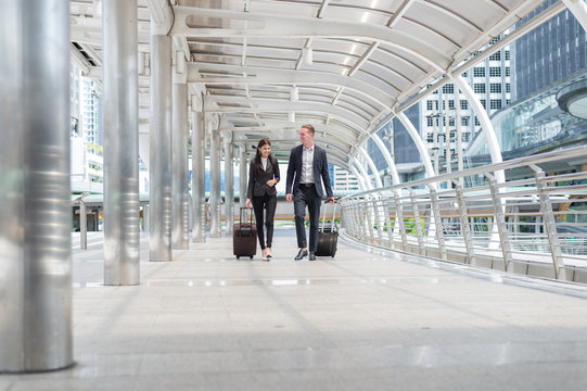 businessman and businesswoman smile and walk together with luggage on the public street, business travel concept