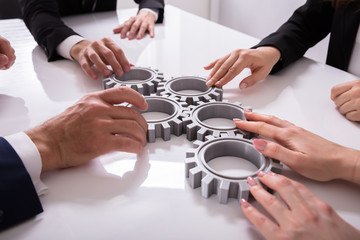 Businesspeople Joining Gears On Desk
