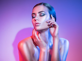 Fashion model woman in colourful bright sparkles and neon lights posing in studio, portrait of...