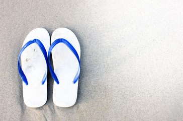 Slipper on the beach, sandals on the beach. Flipflops on a sandy ocean beach - summer vacation concept. Beach summer casual shoes. Copy space