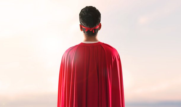 Superhero man with mask and red cape in back position on a sunset background