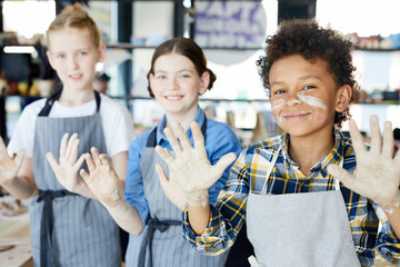 Funny schoolboy with dirty hands and face and two girls on background showing their palms