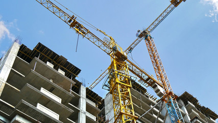 Two cranes near buildings against blue sky. Construction site.
