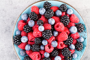 Fresh berry salad on blue dishes. Vintage wooden background.