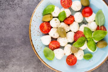 Delicious caprese salad with ripe cherry tomatoes and mini mozzarella cheese balls with fresh basil leaves.