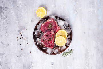 Fresh raw meat beef on a wooden plate with lemon slice and ice. Lean proteins.