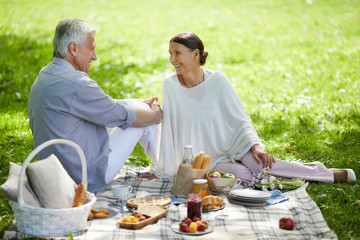 Happy aged female looking at her husband during talk while enjoying sunny summer day and picnic