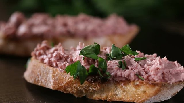 Spreading chopped parsley over liverwurst sandwich on a dark slate - close up view
