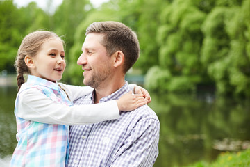 Little girl embracing her father while talking to him during walk in park on summer day