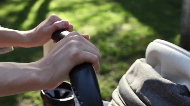 Mother's hand rolls stroller with sleeping baby in summer green park