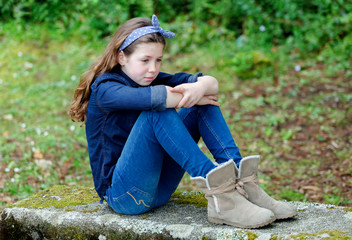 Sad small girl with ten years old sitting on a bench