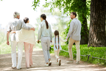 Back view of young family of three and senior couple spending summer weekend in park