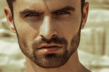 Strong face male model on the nature background with sand and water on the beach on the sunset