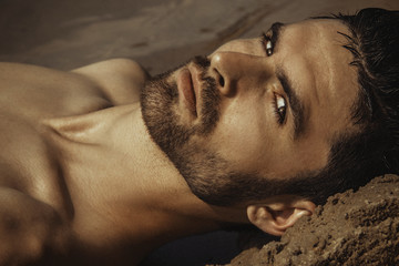 Strong face male model on the nature background with sand and water on the beach on the sunset