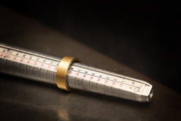 golden ring  on a ring sizer gauge, jeweler sizing tool from steel against a dark background with copy space