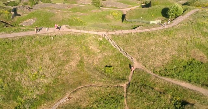 Girl on a rocky coast, C4K aerial rising view above a woman walking on path at the shore of Suomenlinna military fortress island, on a sunny summer evening, in Helsinki, Uusimaa, Finland