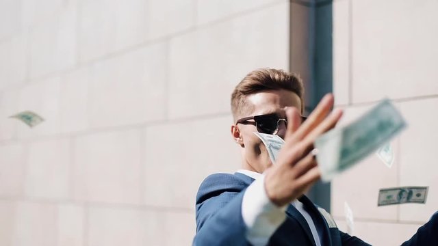 Young happy businessman walking and scatter the dollars on the street near the office center, slow motion. Money rain. Successful business or winning the lottery. Shot on Red Epic