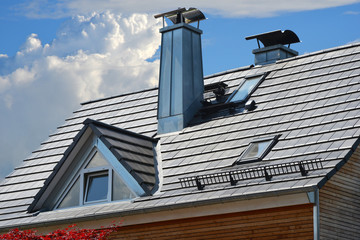Schornsteine mit Zinkblech-Verkleidung und Edelstahl-Schutzdach auf einem grauen Ziegeldach mit...