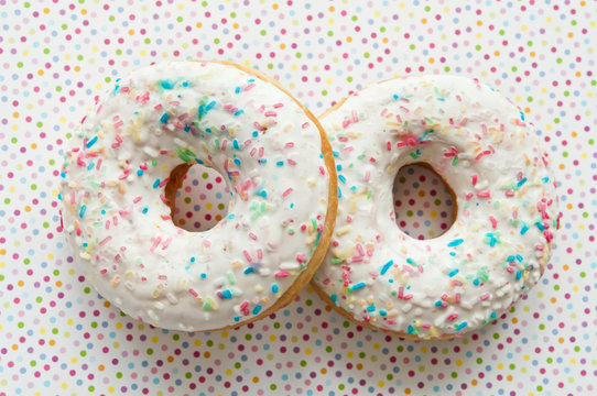 two glazed donuts decorated with colorful sprinkles