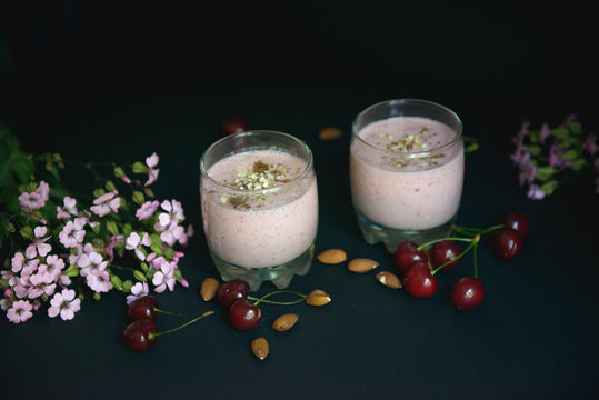 Two Glasses with a beautiful smoothies with nuts and flowers on a black background.