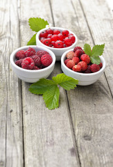 view on three   little bowls on a wooden table full of red berries 