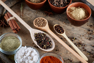 Various spices in wooden spoons and bowls and some salt on an old wooden barrel, top view, close-up, selective focus.