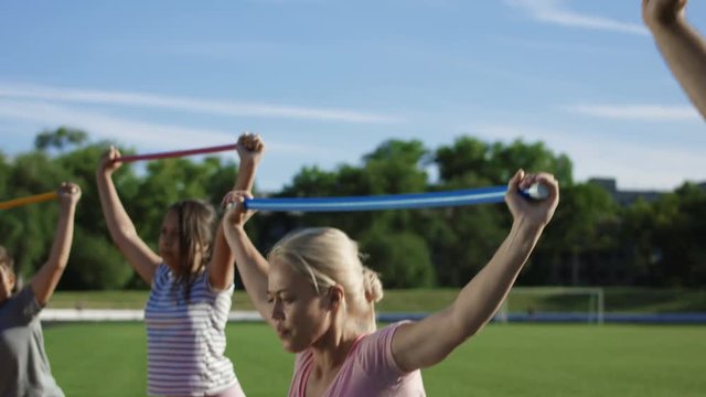 Adult serious woman and children doing exercise with fitness stick on field in summer sunlight